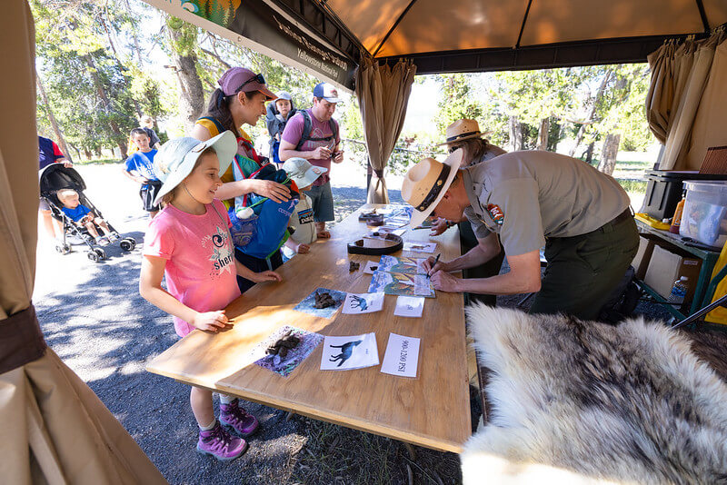 Yellowstone Park rangers signing Junior Ranger booklets for young participants.