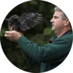 Circular outdoor portrait of John Marzluff holding a black raven.