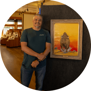 Loren Henderson standing indoors next to a framed painting of a bison with a vibrant yellow and orange background.