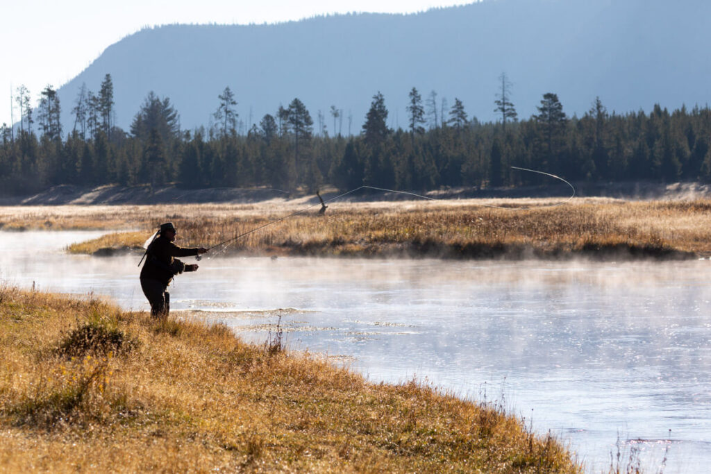 A fly fisherman casts a line over a misty river at dawn.